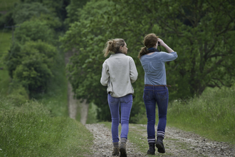 Two women walking down a country lane and looking through binoculars